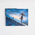 Open hardcover book flat lay displaying full-color endpaper artwork of a figure running along a high bridge under a blue sky